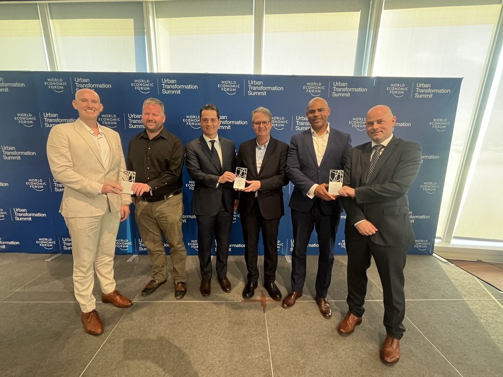 Six people holding awards in front of a World Economic Forum Urban Transformation Summit backdrop